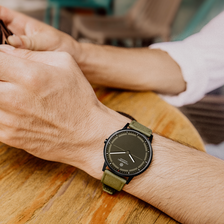 Mate2+ khaki watch on male wrist resting on wooden table